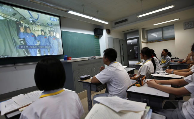 Varios estudiantes siguen por televisión las explicaciones de tres astronautas chinos. Foto: EFE