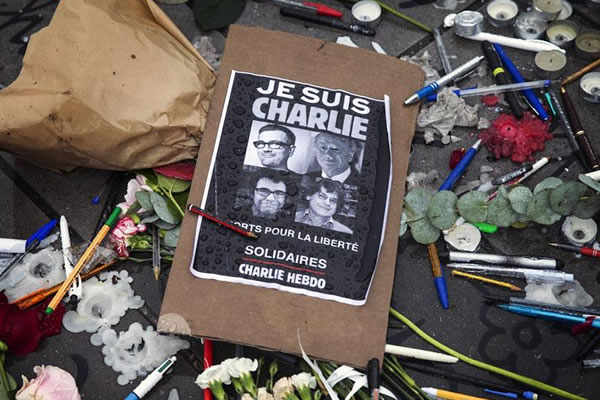 Un cartel en solidaridad con las víctimas, flores, bolígrafos y lapiceros depositados junto a varias personas que guardan un minuto de silencio en la Plaza de la República en París (Francia). Foto: EFE