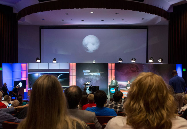 Personas observan imágenes de Plutón durante un programa en directo de la televisión de la NASA. Foto: EFE