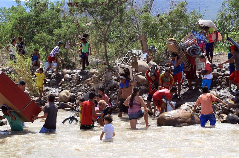 Cientos de colombianos cargan sus pertenencias por el río Tachira desde Venezuela hacia el sector La Parada, Colombia. Foto: EFE