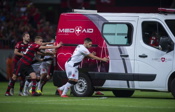 Jugadores de Flamengo y Vasco da Gama empujan la ambulancia fuera del campo de juego. Foto: AFP