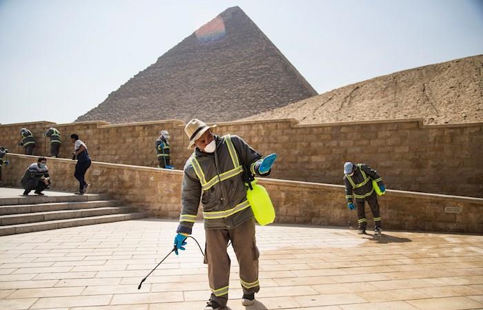 Varias personas desinfectan las inmediaciones de las pirámides de Guiza en El Cairo. Foto: EFE