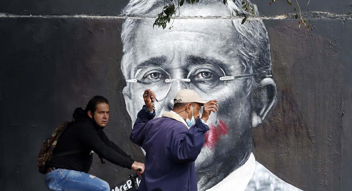 Dos personas pasan junto a un mural del expresidente Álvaro Uribe en Bogotá. Foto: EFE
