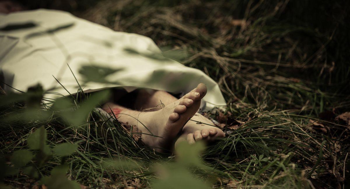 Cuerpo inferior de víctima de asesinato abandonado en el oscuro campo con los pies desnudos sobresaliendo. Foto: Shutterstock